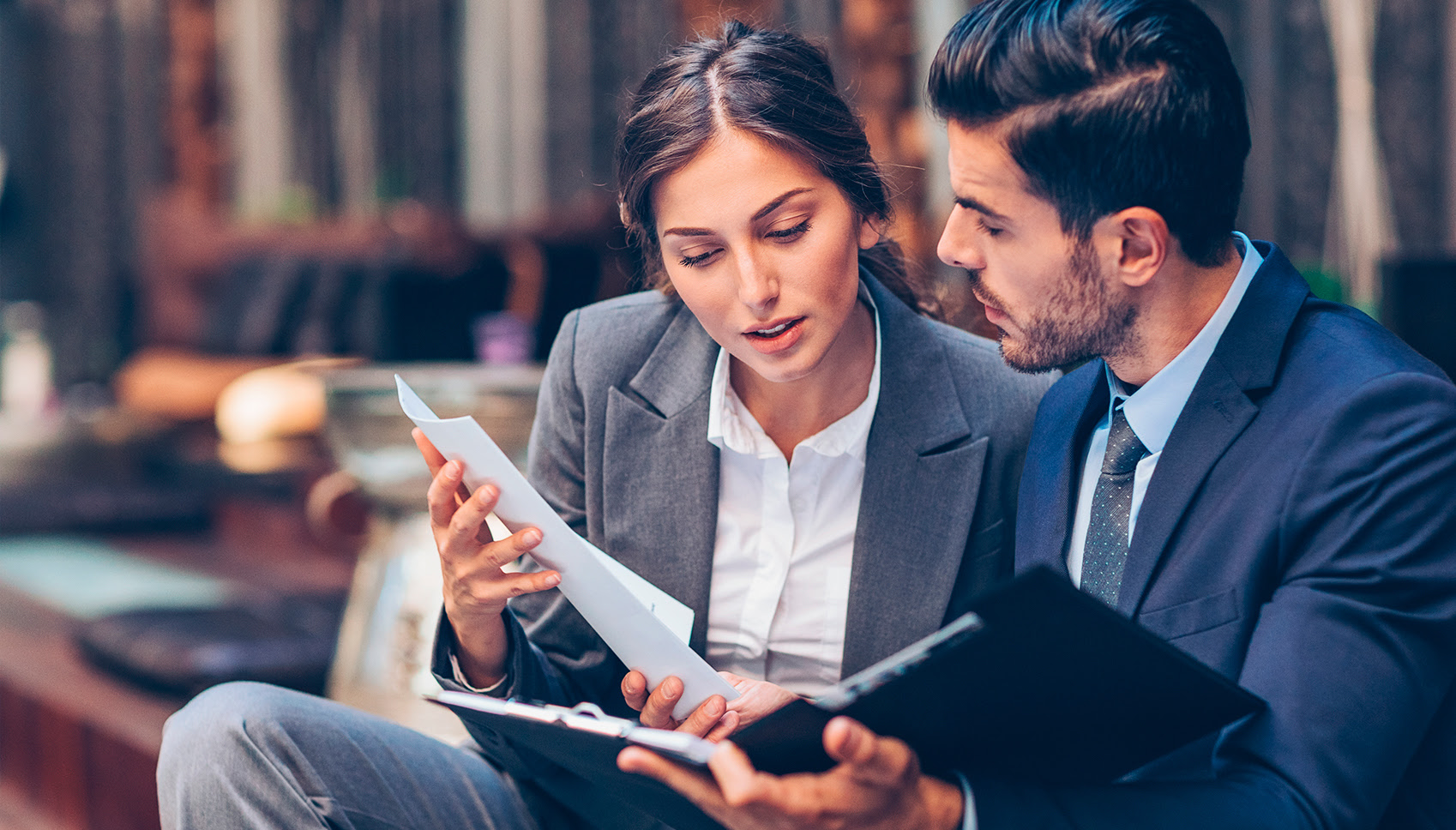 Two workers are looking over paperwork together dressed in business attire.